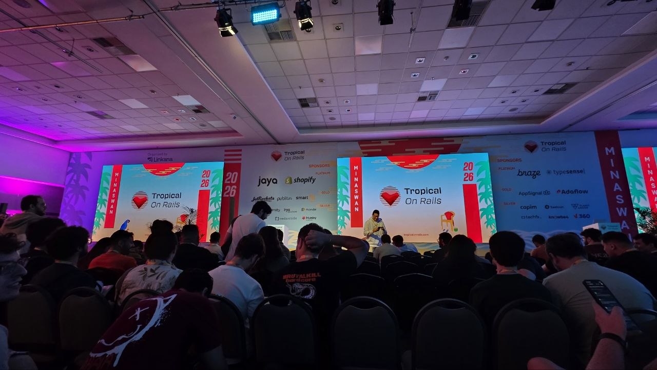 Auditorium at Tropical On Rails 2025, with the lit stage and event logo on screen.